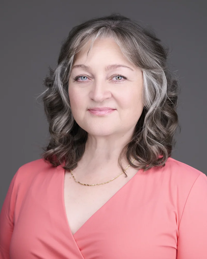 Professional headshot of a woman with silver hair in a warm coral top, photographed in Phoenix by Marie Feutrier
