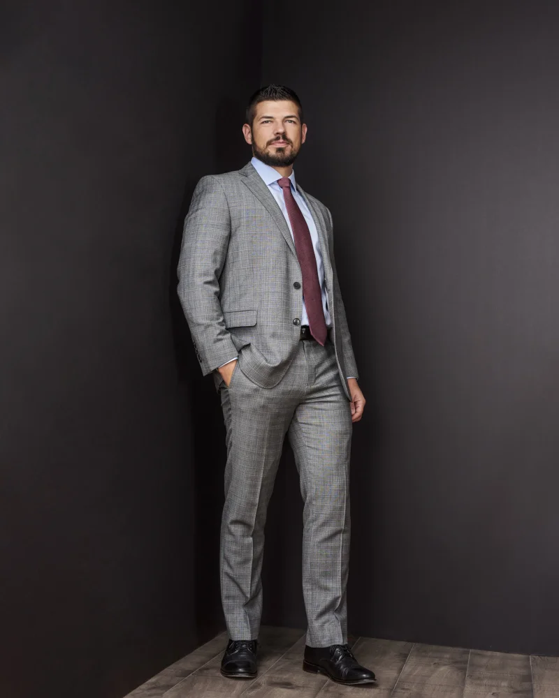 Man in a well-fitted grey plaid suit with burgundy tie demonstrating proper suit fit for a professional headshot