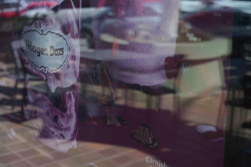 Abstract purple window reflection with the Häagen-Dazs logo caught in the glass and chairs reflected behind it