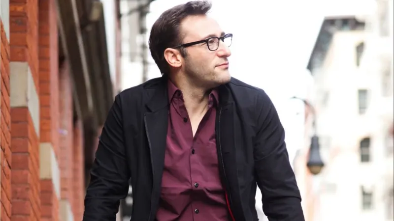 Simon Sinek in a blazer over a casual button-up — professional enough for a keynote, relaxed enough for coffee