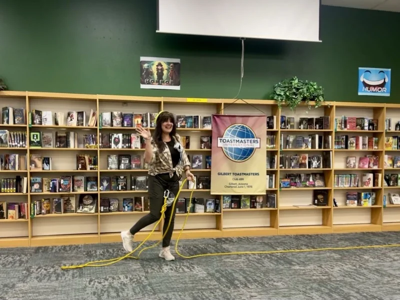 Marie Feutrier crossing the stage at the Gilbert Toastmasters Tall Tale contest with a yellow climbing rope as a prop