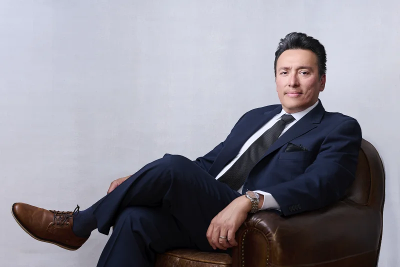 Phoenix executive in a full navy suit and tie seated in a leather chair for an environmental headshot photographed in Gilbert Arizona
