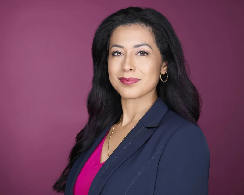 Woman in a navy blazer over a bright pink top against a magenta background showing how a pop of color under a neutral jacket photographs