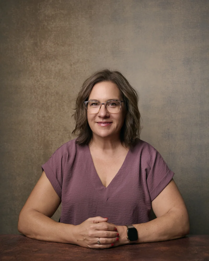 Woman in a relaxed mauve V-neck top seated with hands clasped, showing how a well-fitting casual top photographs in a professional portrait