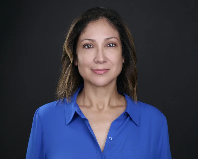 Woman in a solid royal blue button-down blouse with an open collar against a dark background for a professional headshot