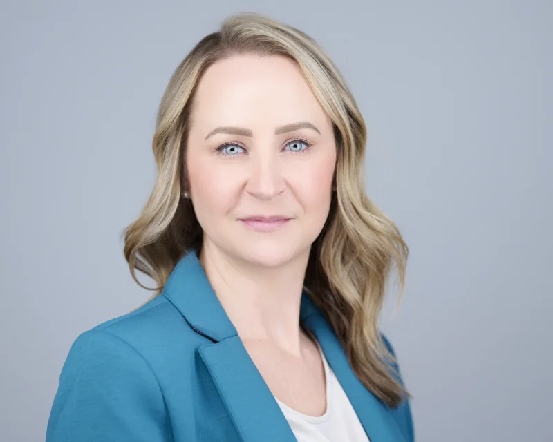 Woman in a structured teal blazer over a white top for a professional headshot against a light grey background
