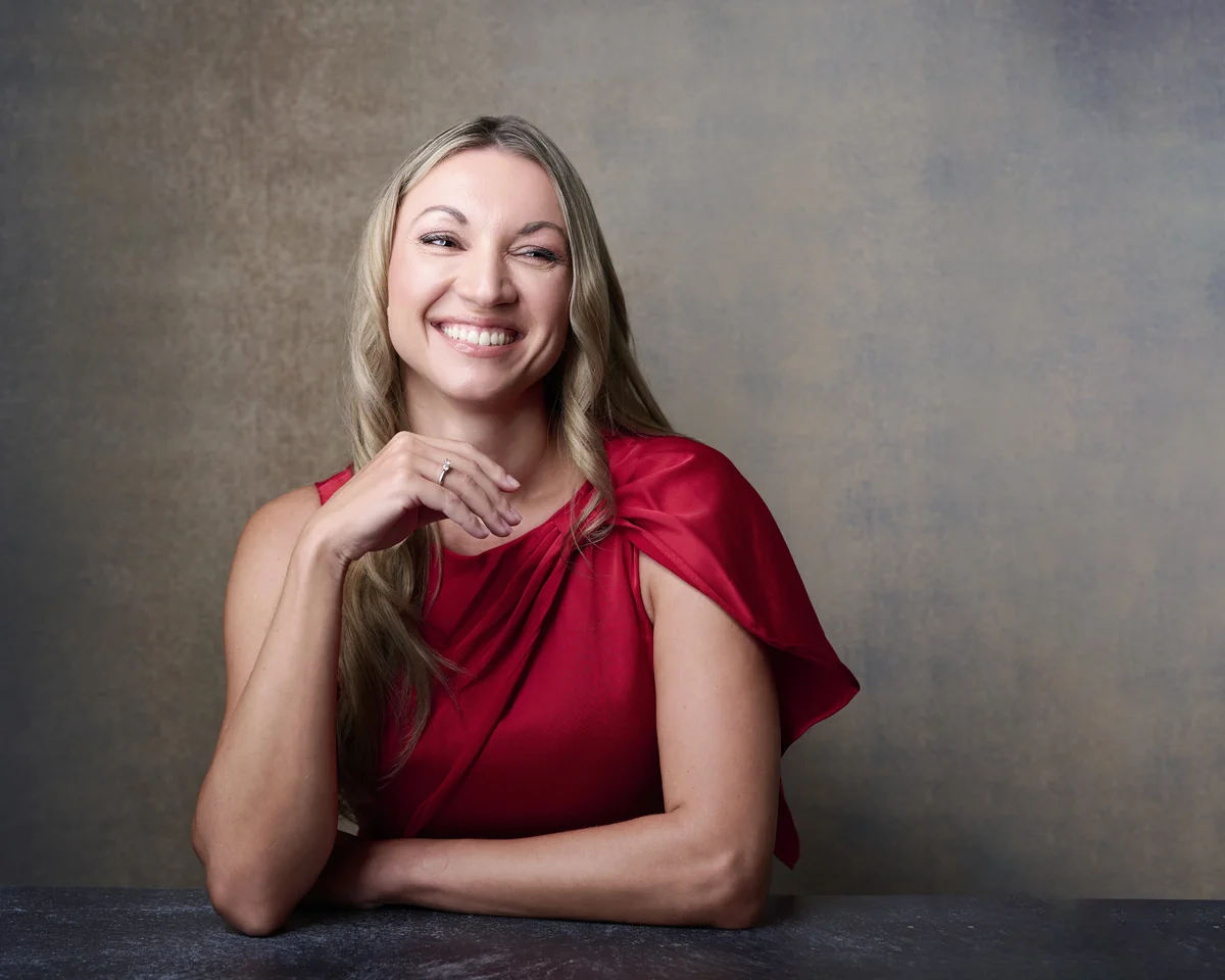 Anna Barnhill leaning on a table in a red silk top, smiling, personal branding portrait against a hand-painted backdrop by Marie Feutrier in Phoenix Arizona