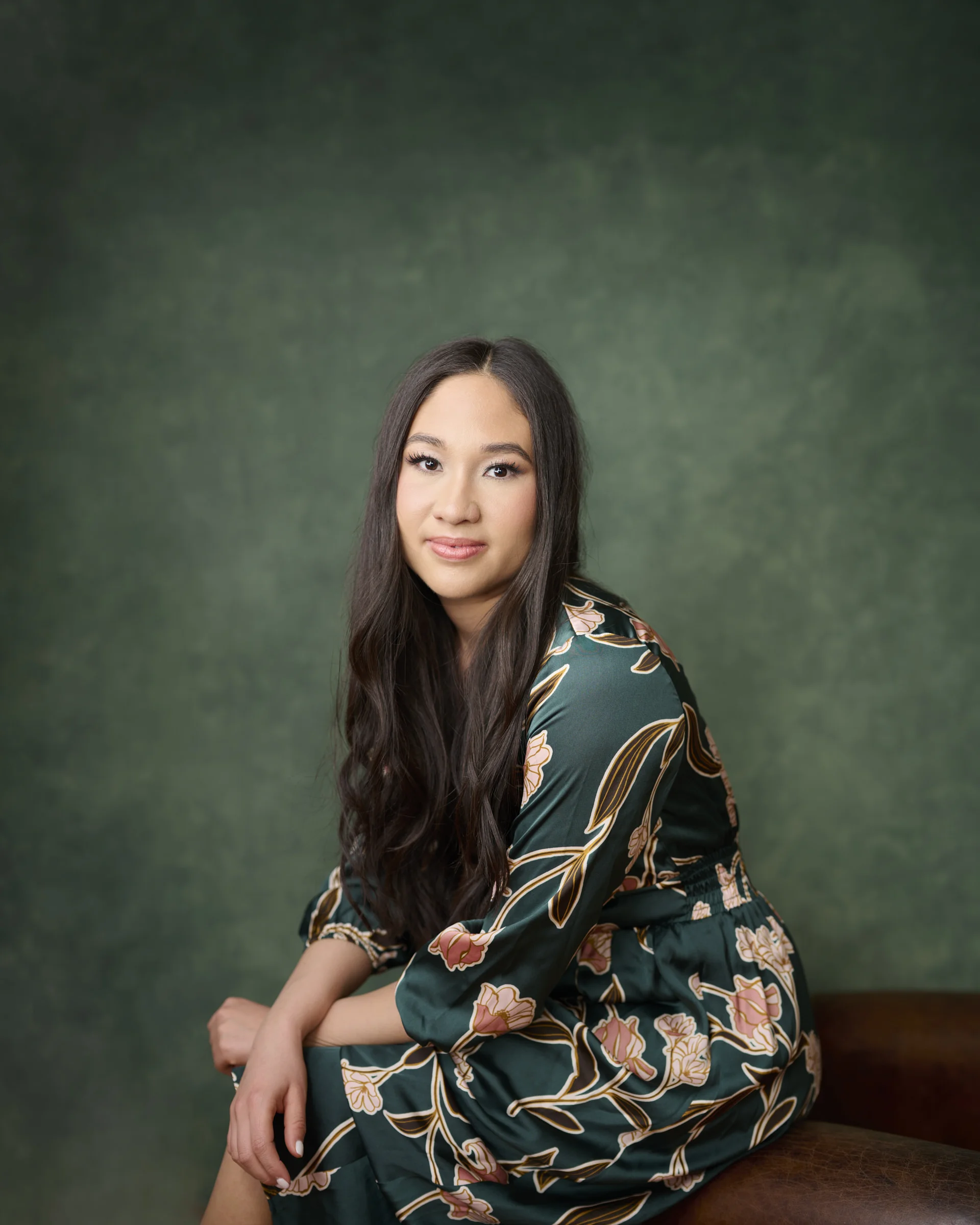 Asian woman in elegant green floral kimono jacket smiling warmly against emerald backdrop