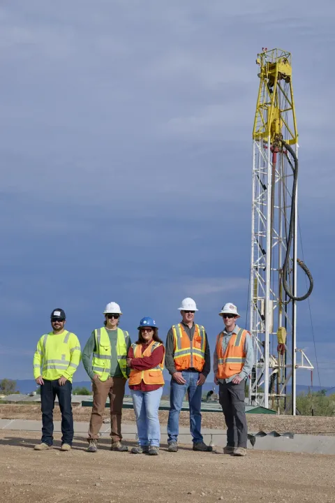 Five oil and gas workers in safety gear and hard hats standing at drilling rig site in Arizona