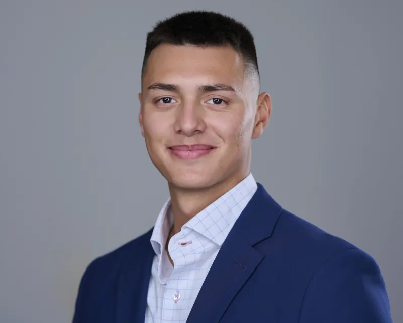 Young man in navy blazer over checked button-down shirt with confident smile ERAS headshot against gray backdrop Phoenix
