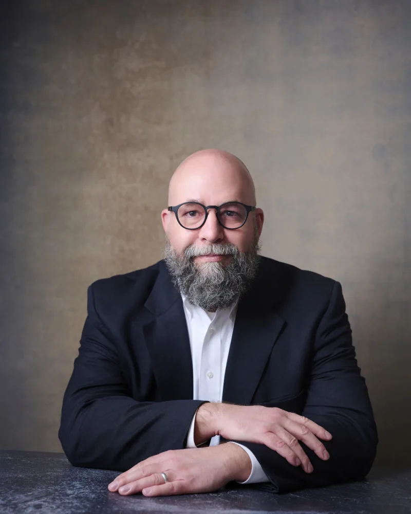 International project management executive portrait with glasses leaning forward against textured backdrop Phoenix Arizona photographer
