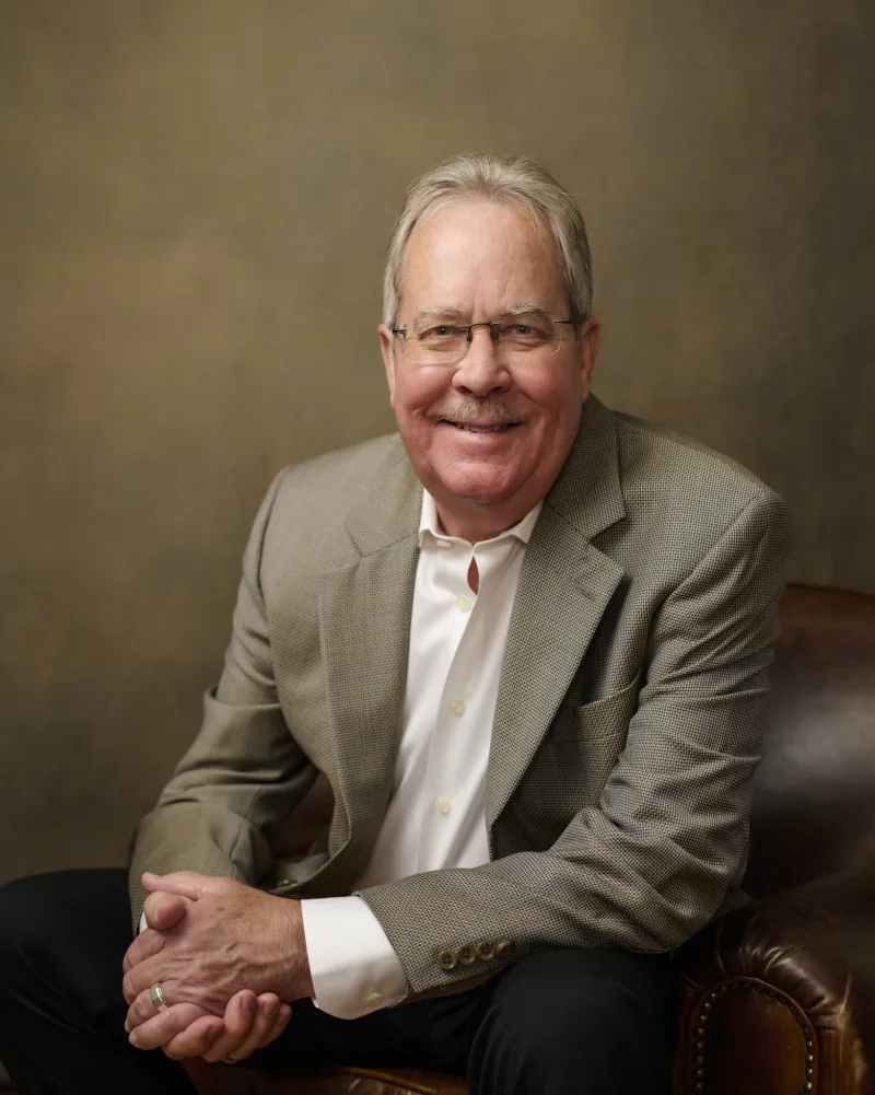 Distinguished senior executive in blazer seated in leather chair warm approachable portrait Phoenix Arizona