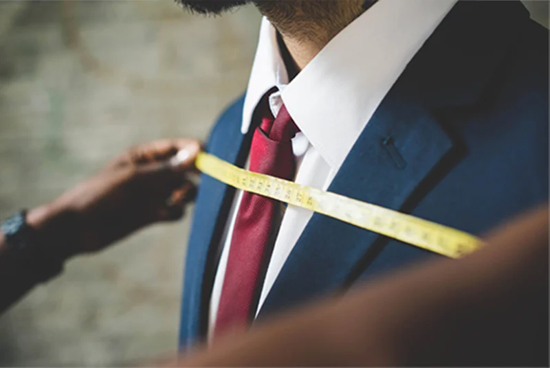 Tailor measuring a man in a blue suit with red tie for a professional headshot session