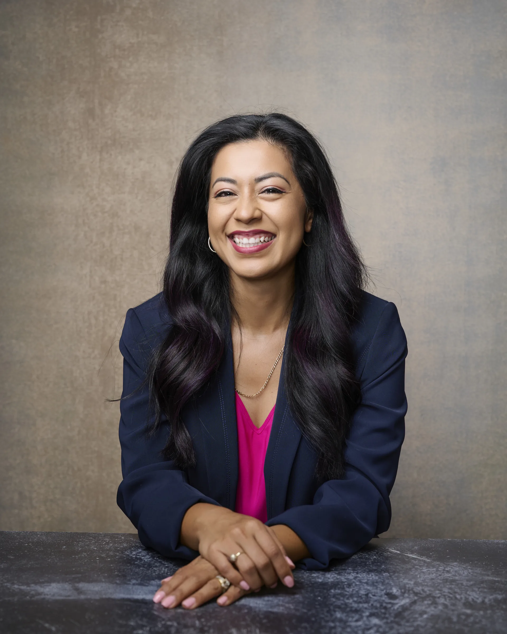 Woman with long dark hair smiling confidently in navy blazer and pink top during professional headshot session