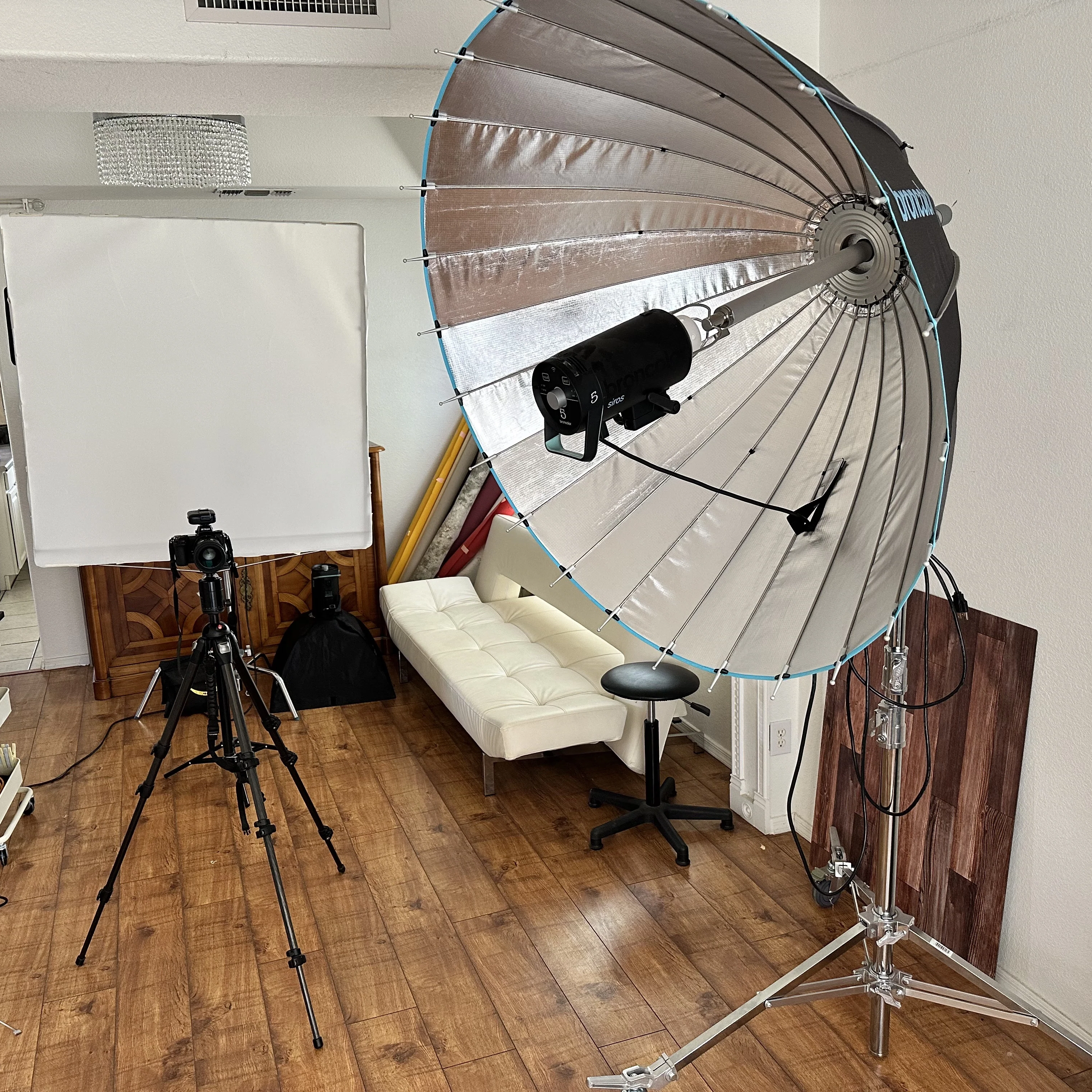 Professional photography studio setup featuring large silver parabolic umbrella modifier, white backdrop, and camera equipment