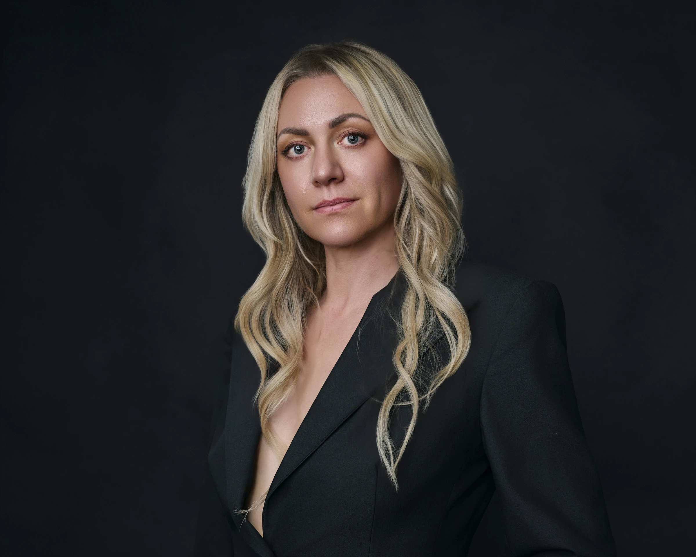 Professional blonde woman in elegant black pinstripe blazer with confident expression against dark backdrop